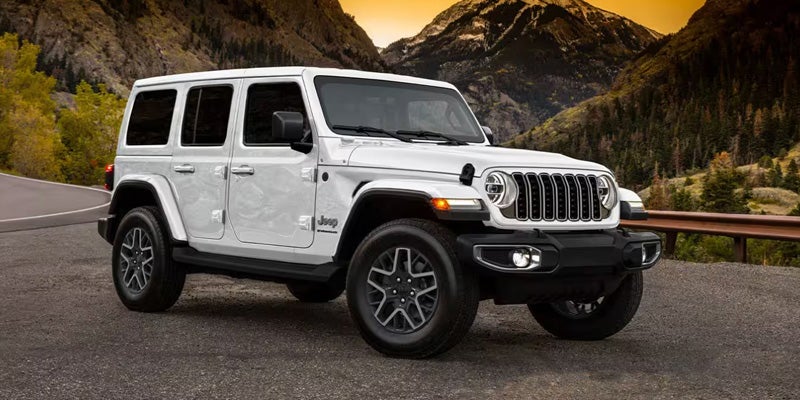 Side angled view of a whtie Jeep Wrangler parked on side of road