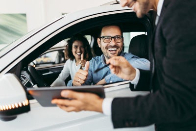 couple in car smiling talking to dealership manager out the window