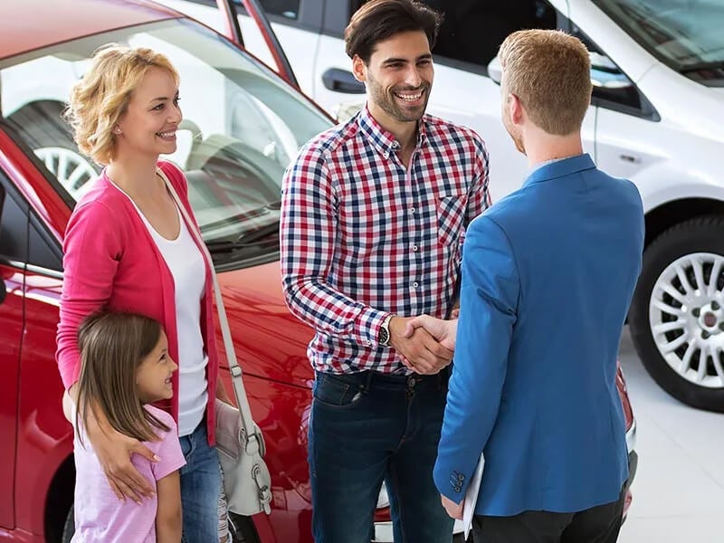 family at car dealership, man shaking hands with car salesman
