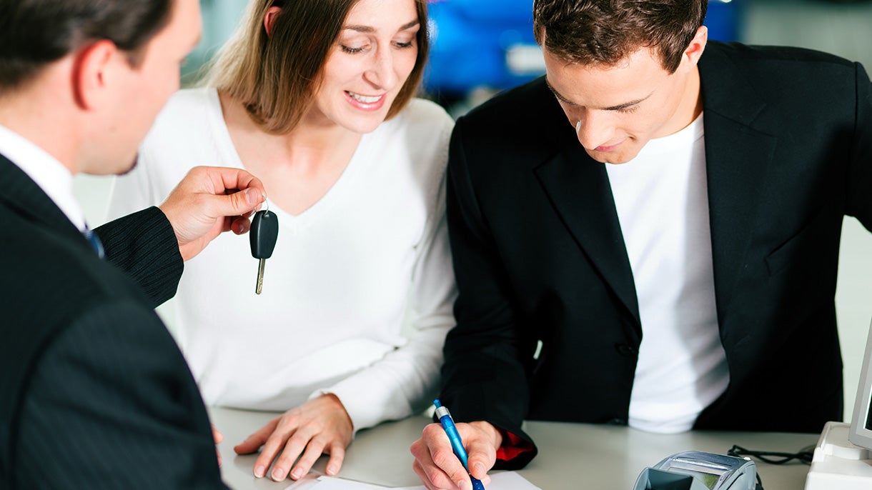 couple signing paperwork at desk, salesman handing them car key