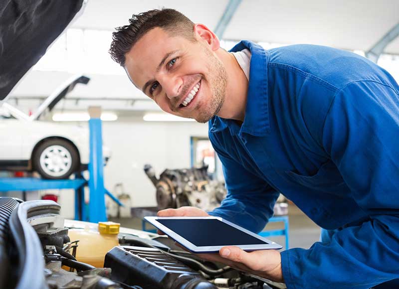 Smiling service mechanic working on a vehicle engine